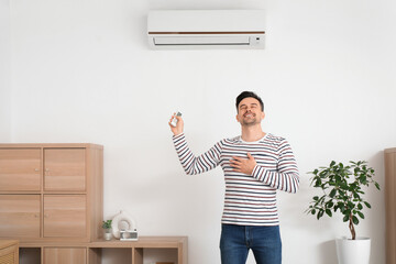 Happy young man turning on air conditioner at home