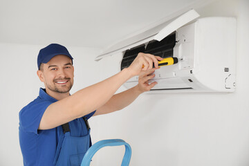 Male technician with screwdriver repairing air conditioner in room