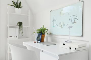 Fototapeta premium Engineer's workplace with wind turbine models and whiteboard in office
