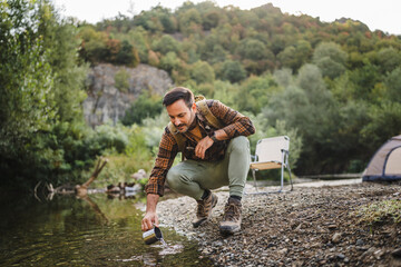 Adult man hiker gathering river water in cup on camping trip