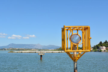 Signal light next to Corfu International Airport in Corfu city, Greece. Island landscape with yellow signal in middle of water with mountain on the background on sunny day.