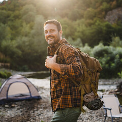 Adult man hiker with a backpack near campsite by river in forest