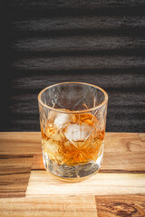 A beautiful glass of wiskey on the Rocks, on a black background, and a wooden table.