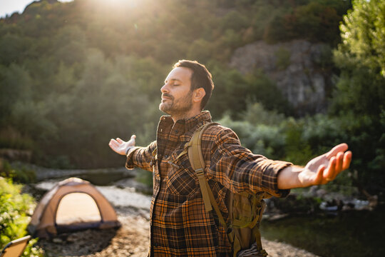 Adult man hiker with a backpack rise up his hands and enjoy the sun
