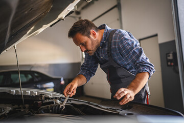 Adult man car mechanic work under car hood in garage with tools in hand