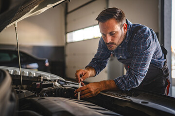 Adult man car mechanic work under car hood in garage with tools in hand