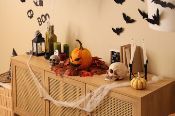 Halloween pumpkin with autumn leaves and candles on commode near beige wall in room