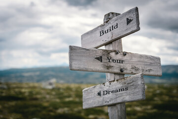 build your dreams text quote on wooden directional signpost outdoors in nature