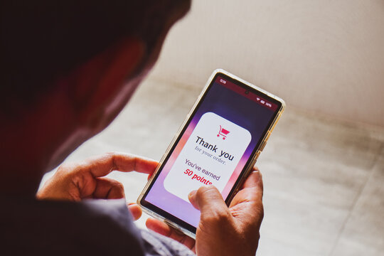 Smartphone screen showing a man earned 50 reward points by shopping online. E-commerce loyalty program concept, selective focus.