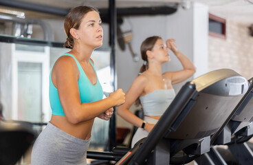 Fototapeta premium Focused motivated young girl leading healthy active lifestyle doing cardio workout in gym, running on treadmill