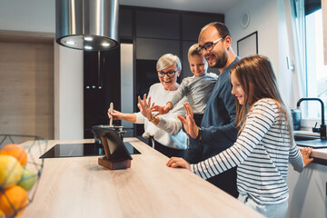 Fototapeta premium Family of four talking to grandparents over a video call, while preparing lunch in the kitchen