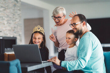 Fototapeta premium Cheerful caucasian family of four communicating with grandparents over video call