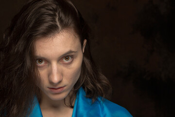 A woman with long brown hair and a blue shirt. She is looking at the camera. Scene is serious and focused