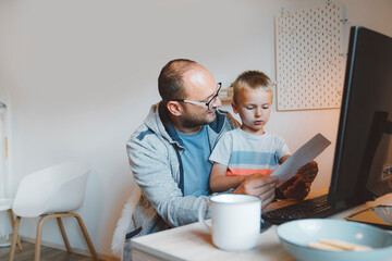 Father helping his son with homework, while doing some of his own work