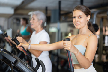 Fototapeta premium Slender athletic girl during cardio exercises on elliptical simulator in fitness center. Sports to max. Electronic tracking for most productive workout