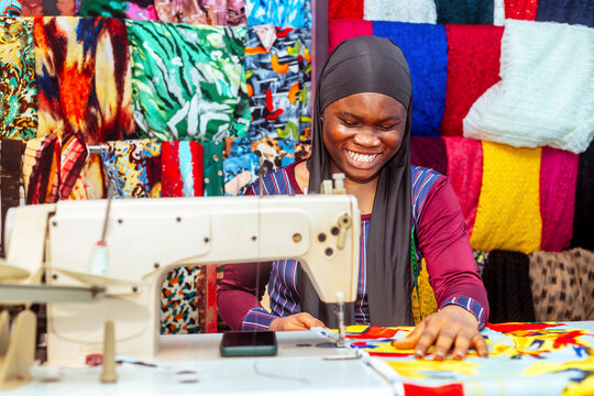 excited african seamstress using modern sewing machine
