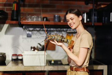 Young woman holding a lobster in a restaurant kitchen and smiling at the camera, focus on fresh seafood concept