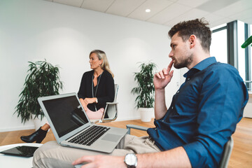 Young businessman with laptop on his lap carefully listening to the training coach