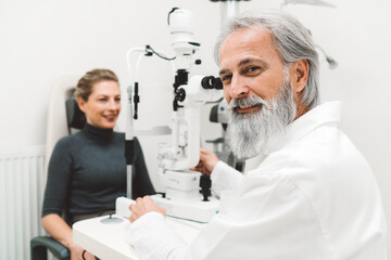 Obraz premium Senior smiling ophthalmologist checking eyesight of a young blonde woman