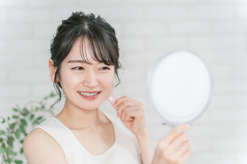 鏡を見ながらかっさでフェイスマッサージをするアジア人女性
