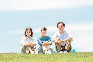 青空の見える公園・丘に座る家族・親子（父親・母親・娘）
