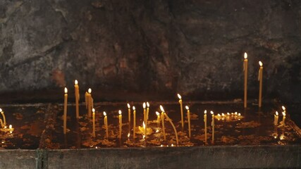Burning church candles in ancient stone altar inside Greek Orthodox monastery. Yellow and orange candles for worship and prayer lighting the small altar inside a mountain in Montenegro
