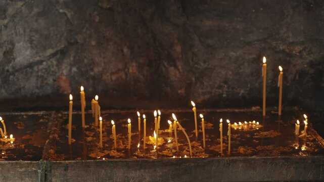 Burning church candles in ancient stone altar inside Greek Orthodox monastery. Yellow and orange candles for worship and prayer lighting the small altar inside a mountain in Montenegro
