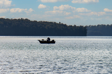 silhouette of man fishing in small boat on northern lake