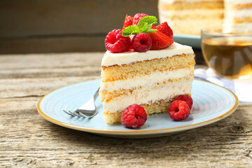 Piece of tasty sponge cake with fresh berries and mint served on wooden table