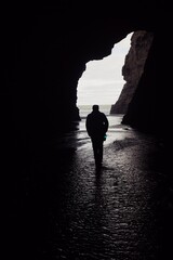 Fototapeta premium Silhouette of a man walking through a cave with an opening to a beach in Piha, Auckland, New Zealand.