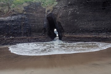 Keyhole in the rock with ocean surf crashing through it at  Piha, Auckland, New Zealand.