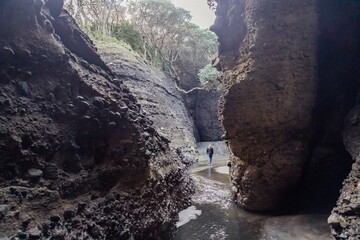 Rocky interior of a cave on the beach with a river flowing through it. Piha, Auckland, New Zealand.