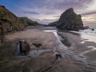 Sandy beach and rocky cliff at low tide with pools and reflections in the sand at sunset. People...