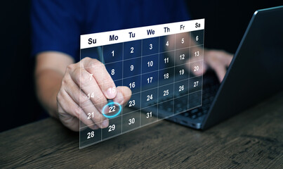 Planning and time management concept. A man manages his time using calendar on virtual screen interface, using his stylus to highlight the date to remind him about important work, meeting, or agenda