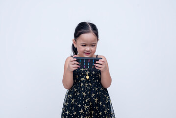 A cute little asian girl in a starry black dress engrossed in playing online video games on a...
