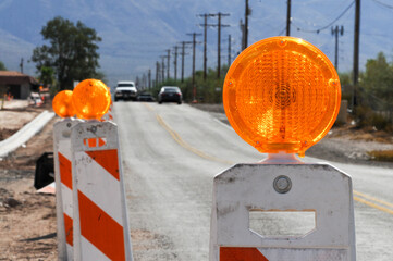Close-up of a construction barricade with a bright orange warning light, set along a rural road...