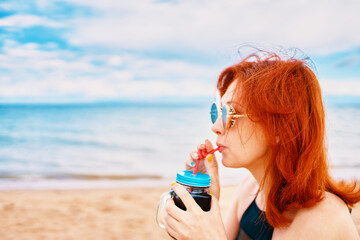 A woman is savoring a refreshing cold drink at the beach, fully embracing relaxation and the sunny atmosphere