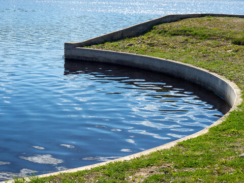 Curved coastline. Landscape with a pond in the park. Water surface with small waves. Prevention of coastal erosion. Concrete edge on the river bank