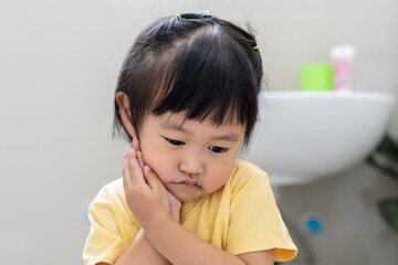 little asian girl presses hand to cheek, suffers from pain in tooth. Teeth decay, dental problems, child emotions and facial expression, oral health care, reducing sweets, fluorine coating.