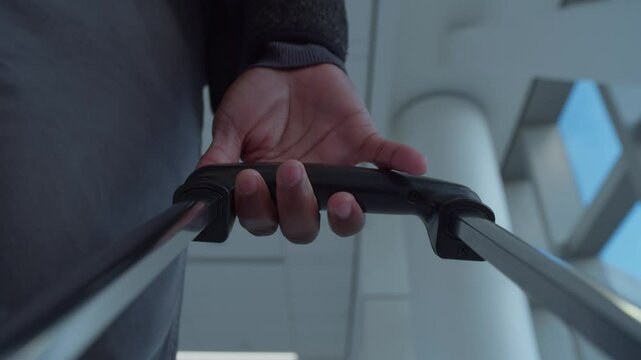 Male traveler dragging a rolling suitcase and stopping at a terminal in a modern airport