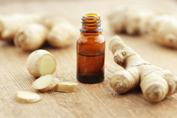 Ginger essential oil or extract in glass bottle with slices of root on wooden background, closeup,...