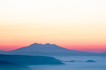 オレンジ色のグラデーションの空と遠くの山のシルエット。少し霞んだ雄大な自然の美しさ。