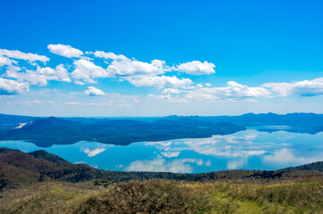 雲の浮かぶ青空を反射する湖と周囲の山々を見下ろす。爽快で清々しい晴れやかな自然の景色。