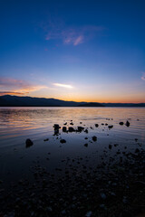 Fototapeta premium 鮮やかなグラデーションの空の色を湖面に反射する夕暮れの湖。岸辺からのローアングル。北海道の屈斜路湖。