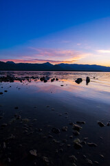 Fototapeta premium 鮮やかなグラデーションの空の色を湖面に反射する夕暮れの湖。岸辺からのローアングル。北海道の屈斜路湖。