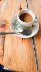 Portrait of coffee with milk in a white cup with a green pattern equipped with a saucer and a small spoon. Photographed with a wooden table as a background.