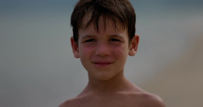 Young boy looks directly into camera with smirk on tropical beach - close up on face