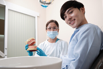 Asian female dentist explaining orthodontic care and whitening to young male patient with teeth...