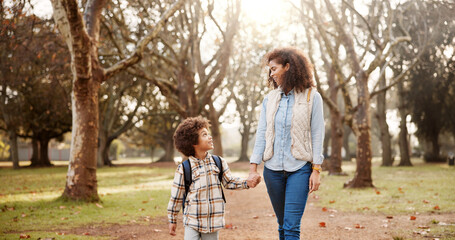 Fototapeta premium Holding hands, mother and child walking to school with safety, bonding and backpack in park together. Happy, woman and son on outdoor garden path for morning commute with love, trust and support.
