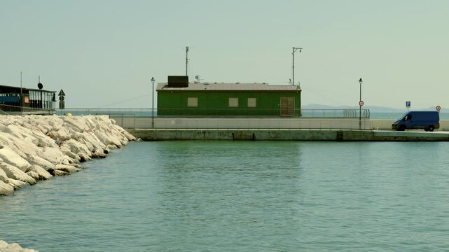 Van parked on a pier by the sea with a green building in the background under a clear sky